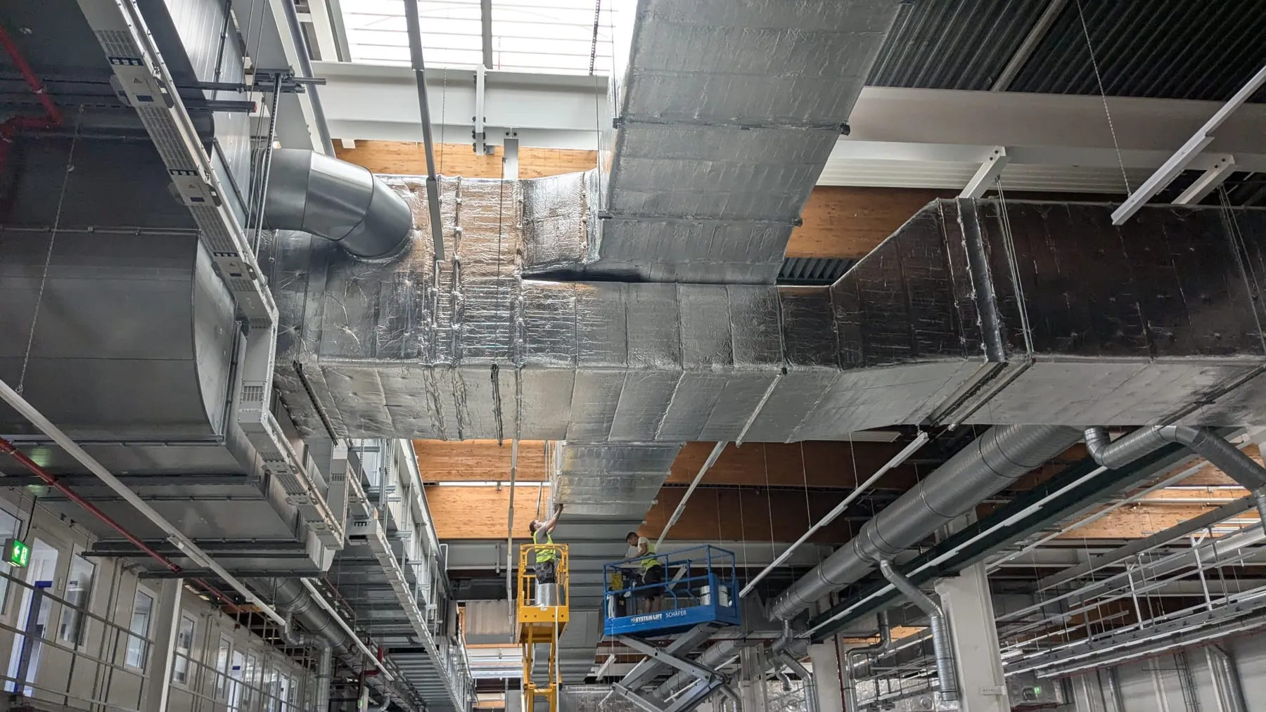 Monteure dämmen Lüftungskanäle in einer Industriehalle